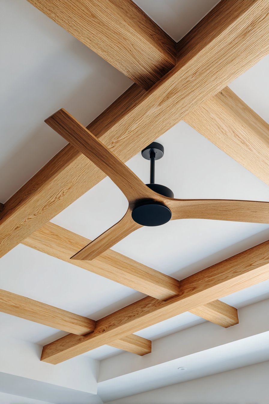 Light oak ceiling beams on a white ceiling with recessed lights and a black fan with wooden blades