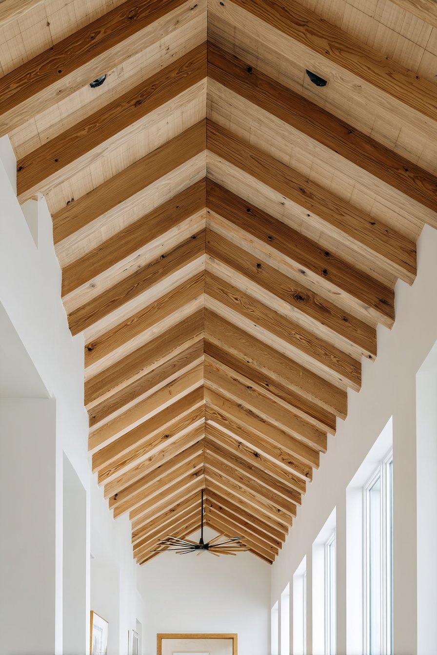 Light oak ceiling beams on a white ceiling with recessed lights and a black fan with wooden blades