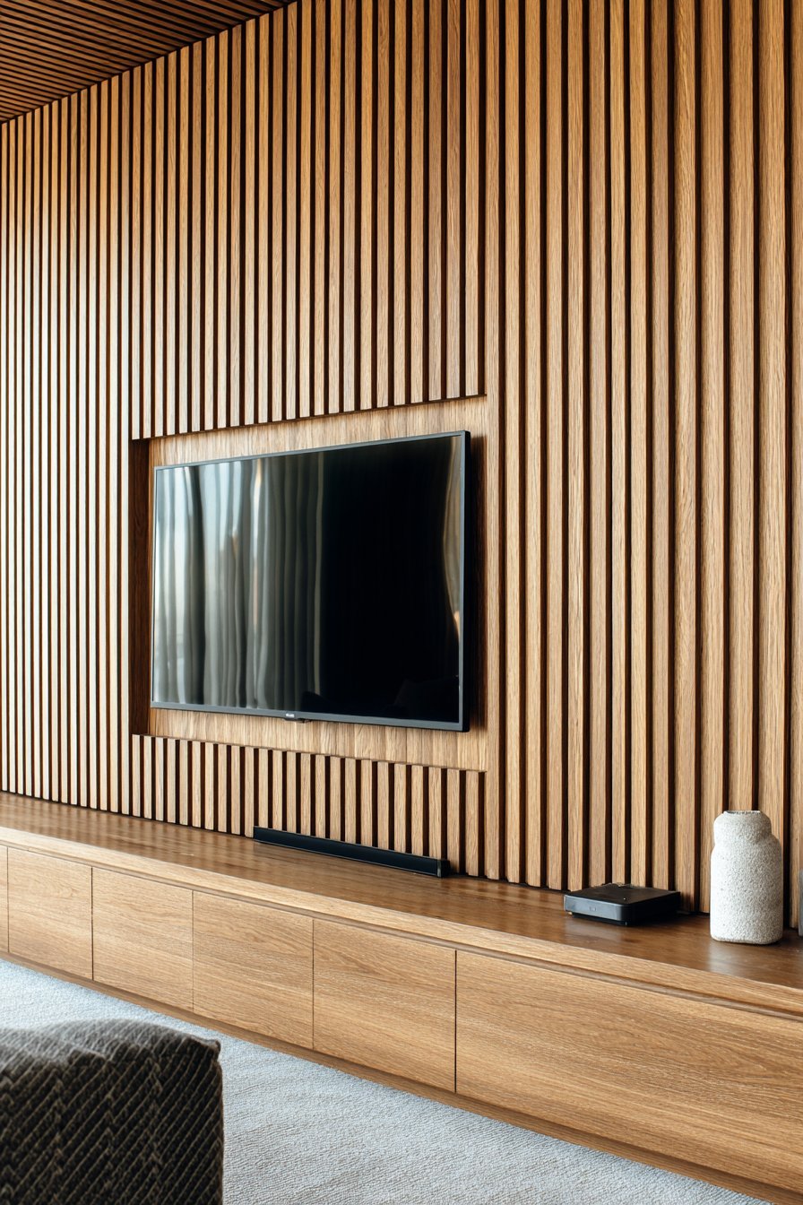Floor-to-ceiling horizontal oak slat wall with LED backlighting above a matching media console
