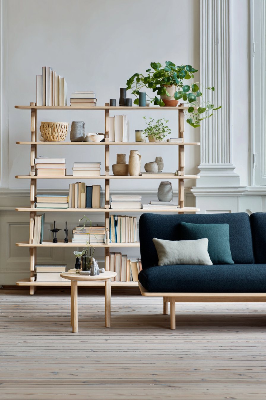Light birch modular shelving divider with books and baskets behind a navy linen sofa under skylights