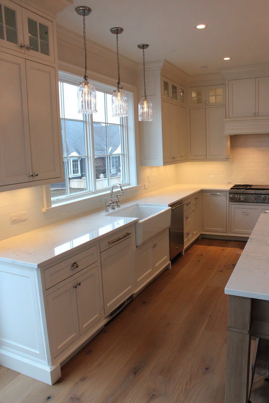 Floor-to-ceiling greige shaker cabinets with white quartz, apron sink, plantation shutters and island breakfast bar