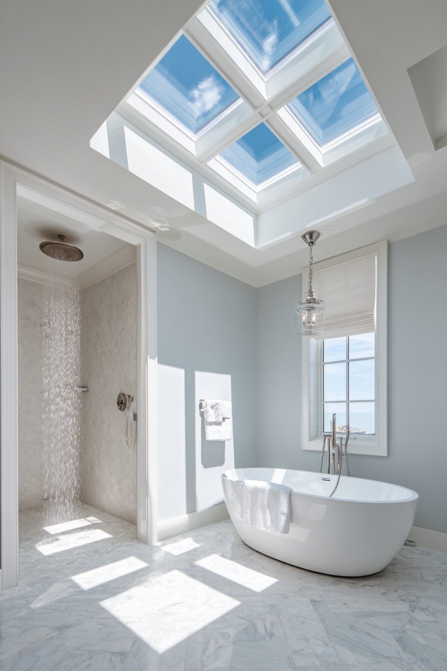 Skylight above a freestanding bathtub with white coffered ceiling, grey walls and rain shower