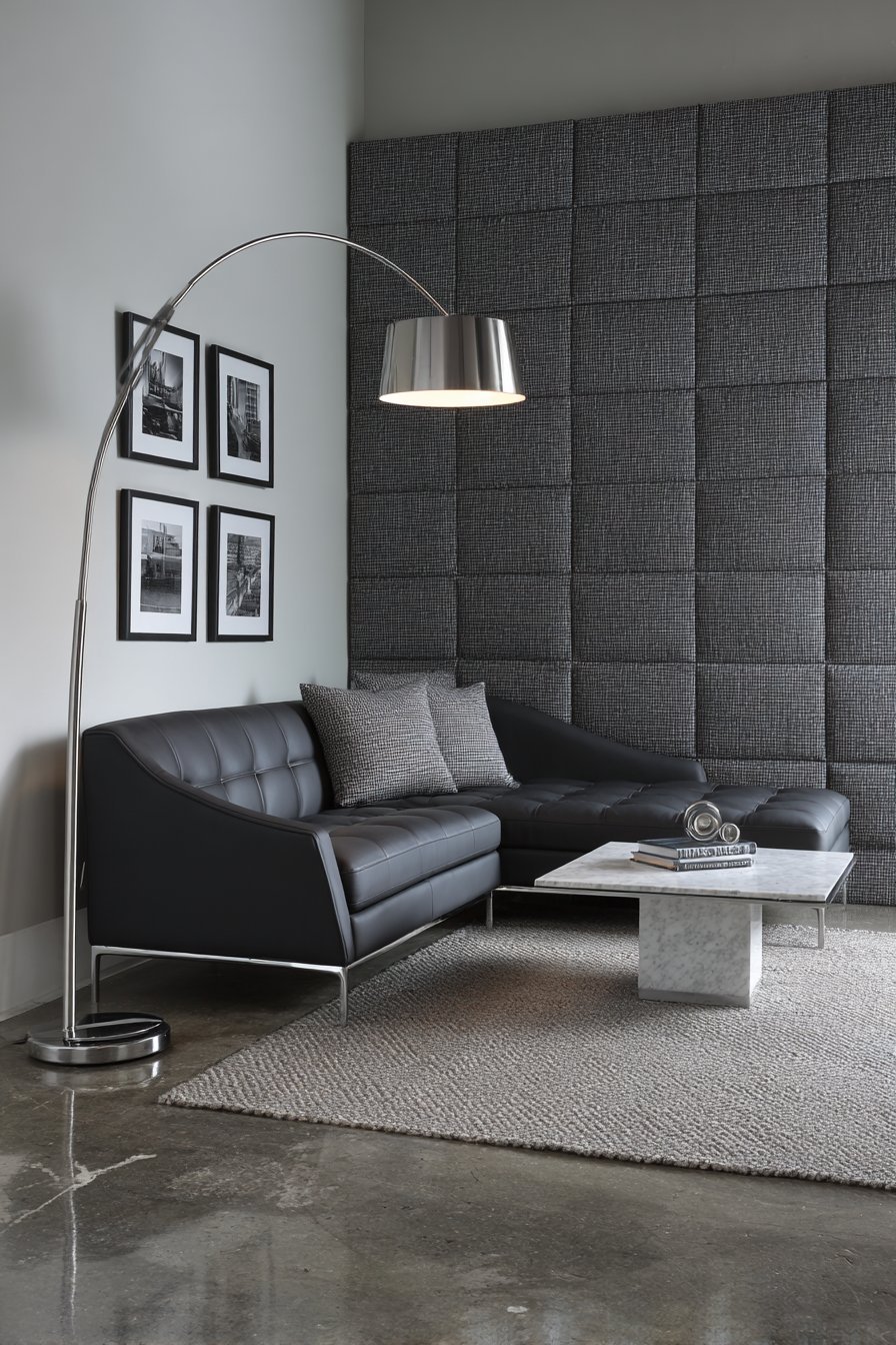 Grey herringbone wool-upholstered walls with black leather sofa, white marble coffee table and concrete floor