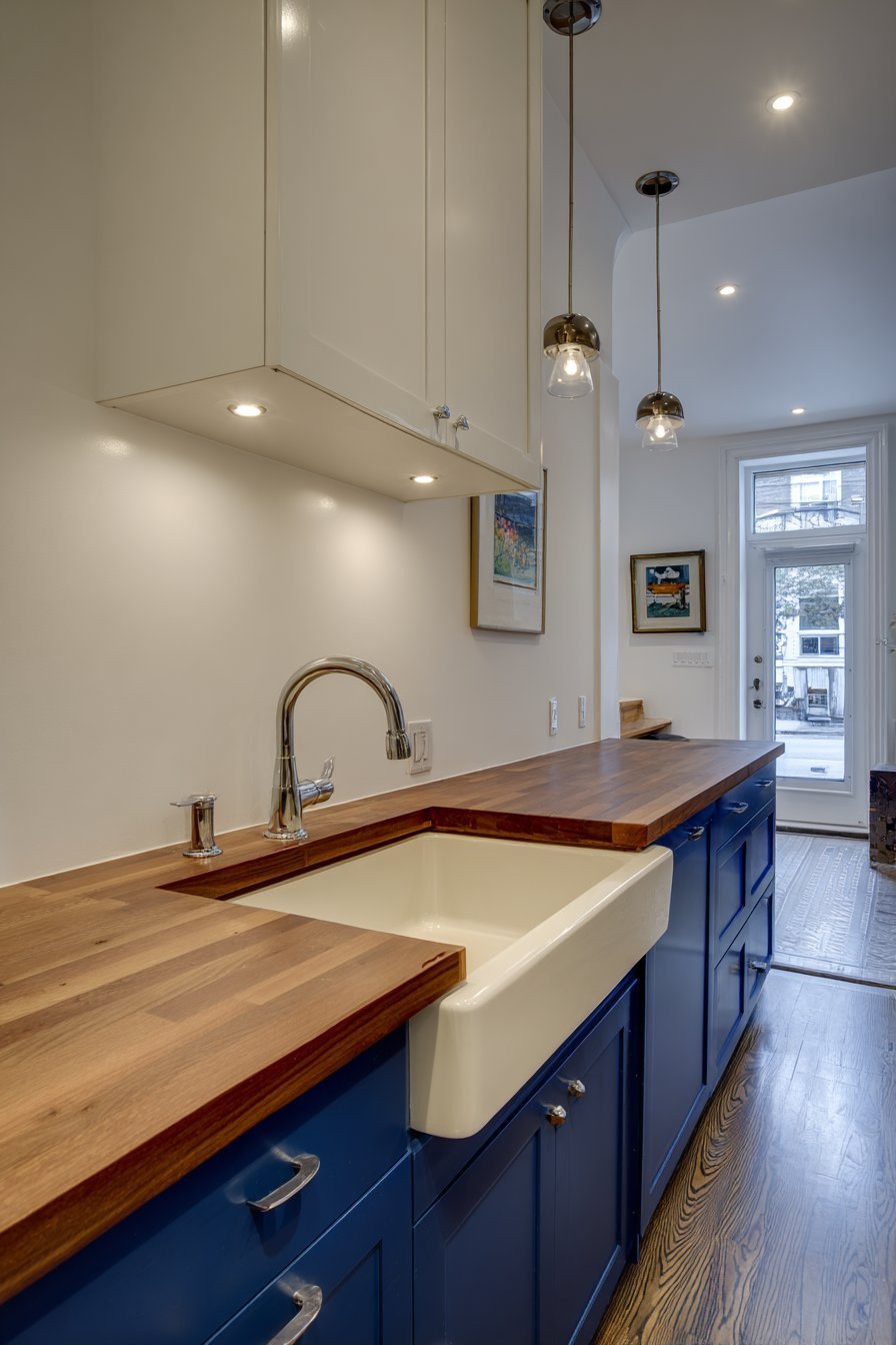 Galley kitchen with navy lower cabinets, white uppers, butcher block counters and pendant lights