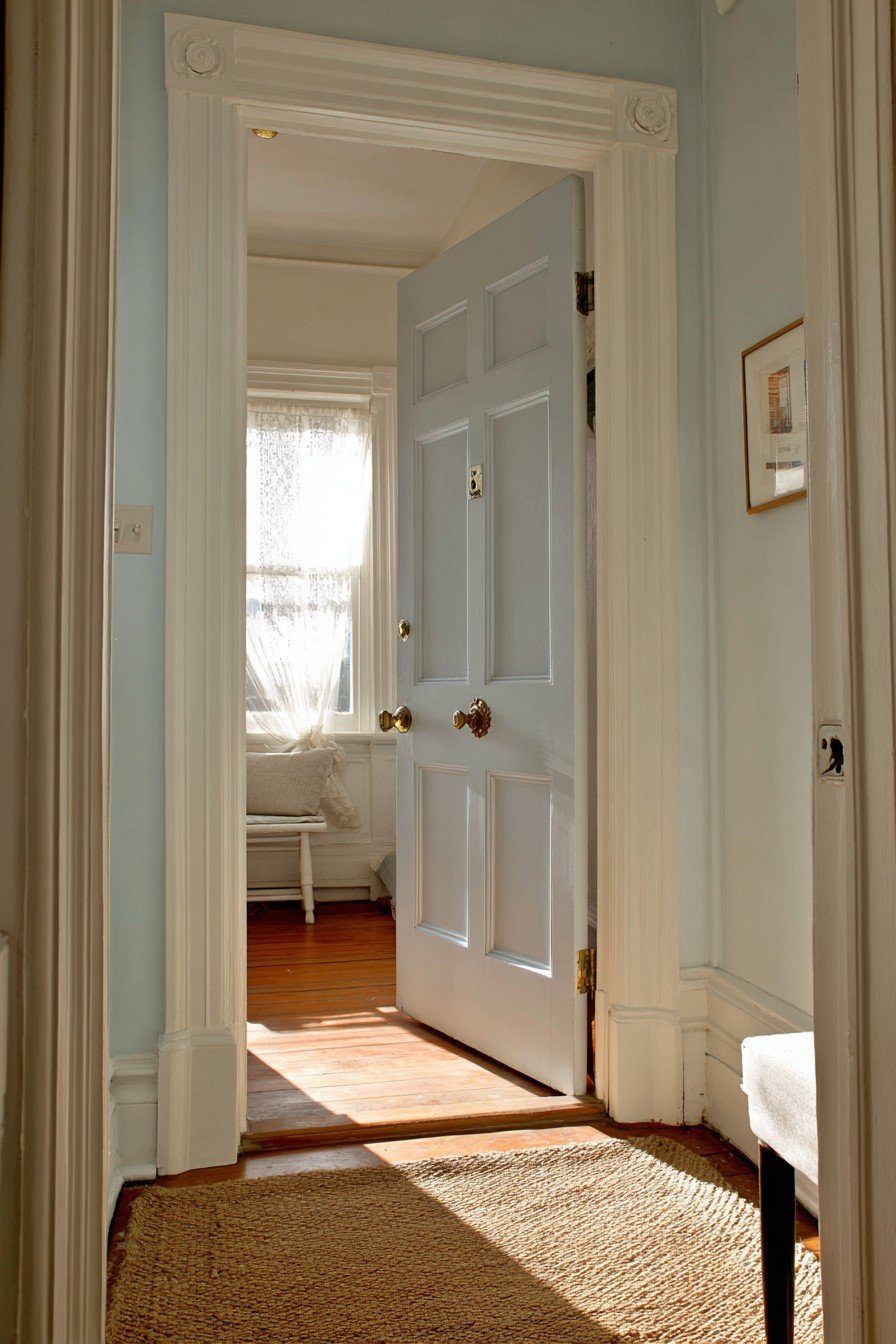 Dove grey six-panel bedroom door with brass knob, white molding, pale blue walls and jute runner