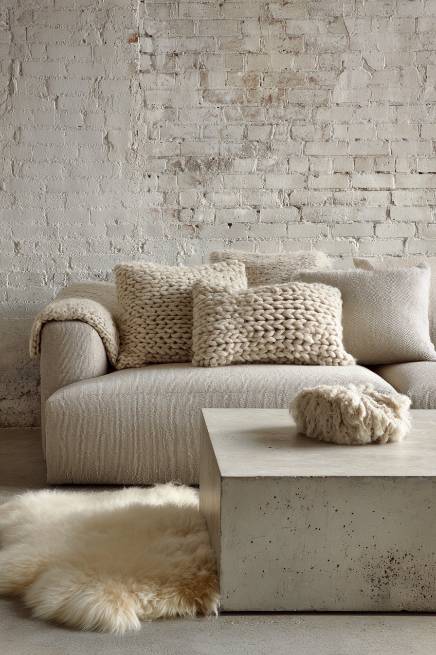 Textural neutral living room with putty grey linen sofa, concrete coffee table, whitewashed brick and sheepskin rugs