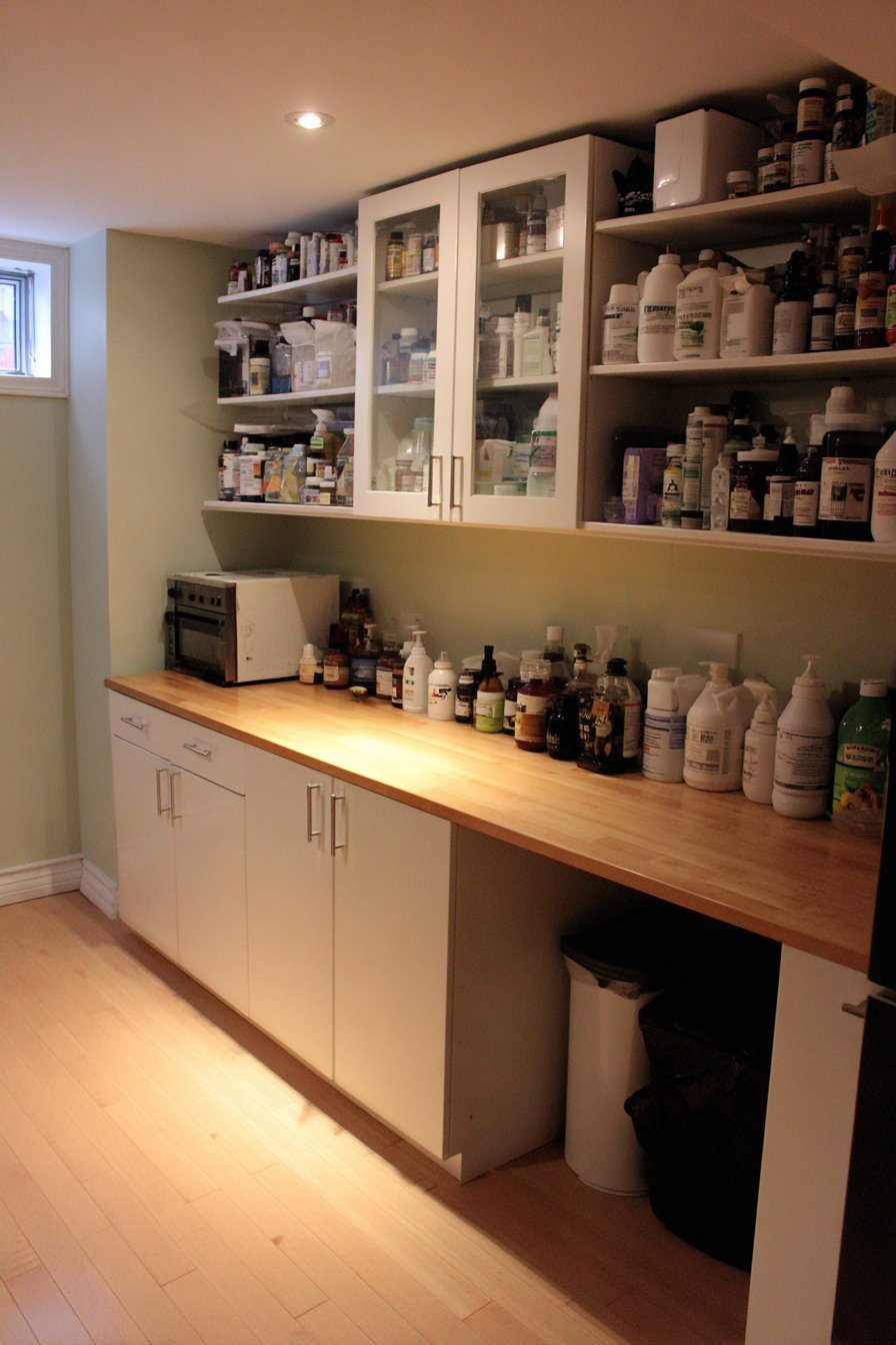 Repurposed white kitchen cabinets with glass-front uppers and butcher block counter on grey-blue basement walls