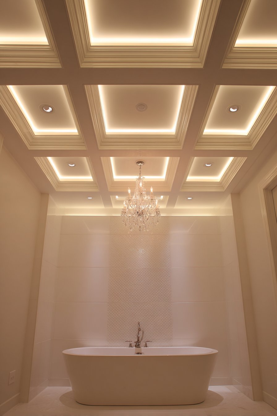 Coffered white ceiling with LED strips above a freestanding tub and chandelier