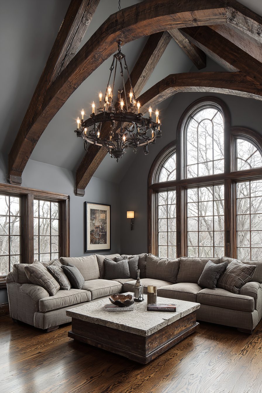 Vaulted ceiling with dark wood beams, slate grey walls, taupe sectional, stone coffee table and iron chandelier