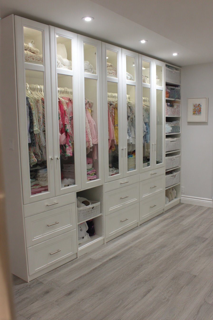 White wardrobe storage system with hanging rods, drawers, glass doors and interior LED lighting in a basement