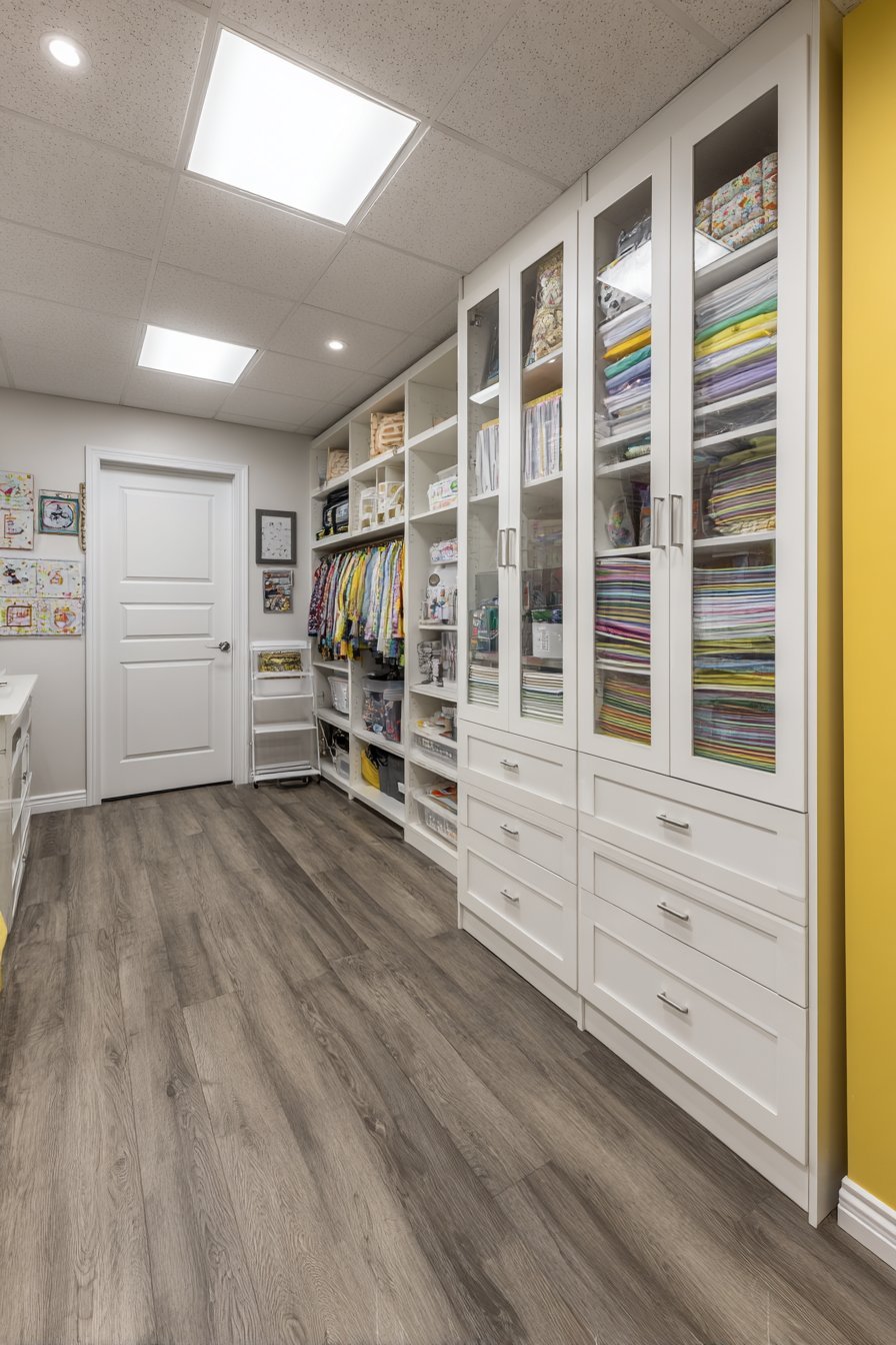 White wardrobe storage system with hanging rods, drawers, glass doors and interior LED lighting in a basement