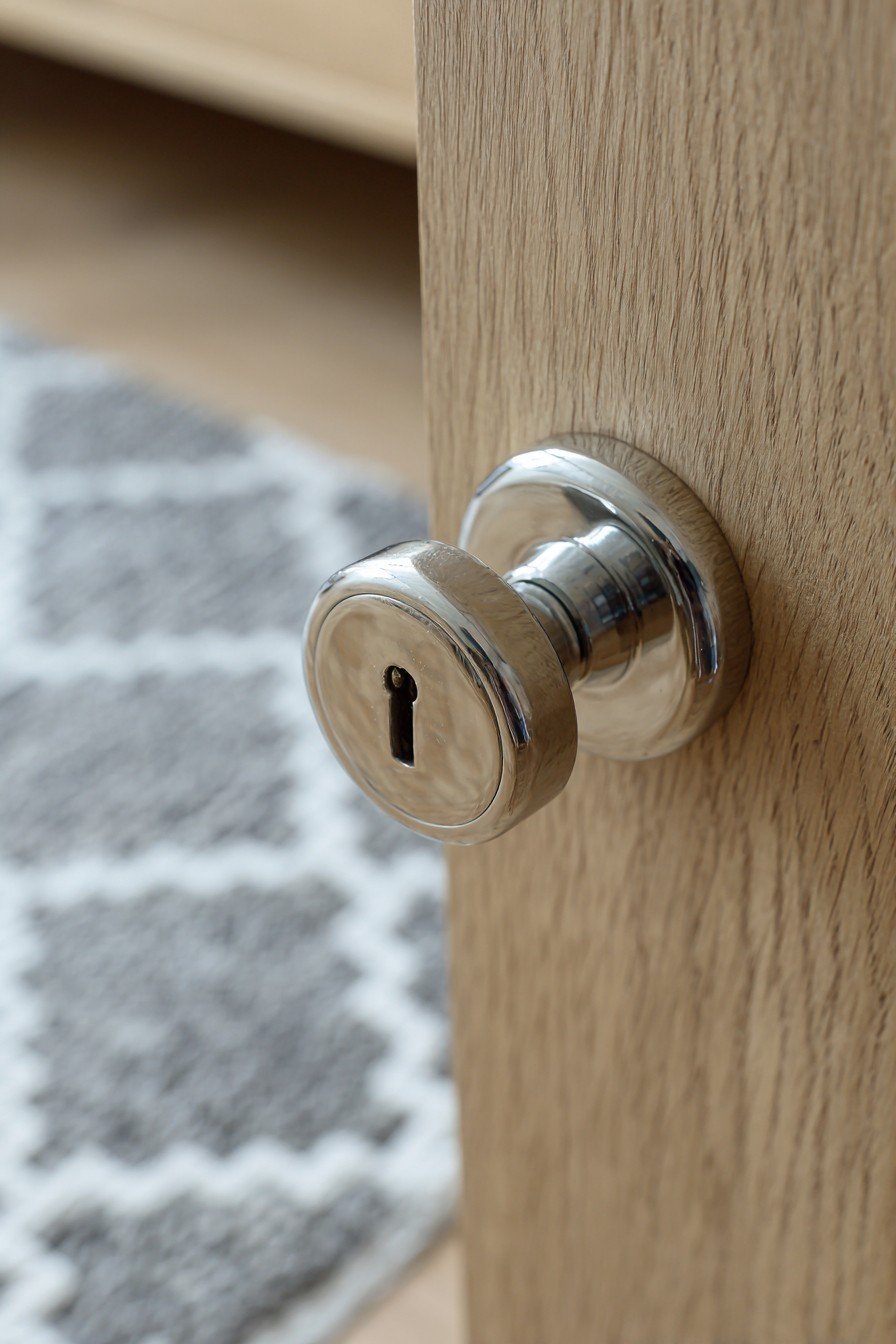 Flush light oak bedroom door with chrome lever handle beside a platform bed and white oak floor