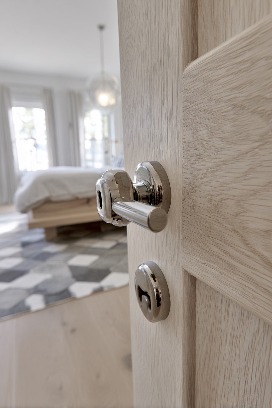 Flush light oak bedroom door with chrome lever handle beside a platform bed and white oak floor