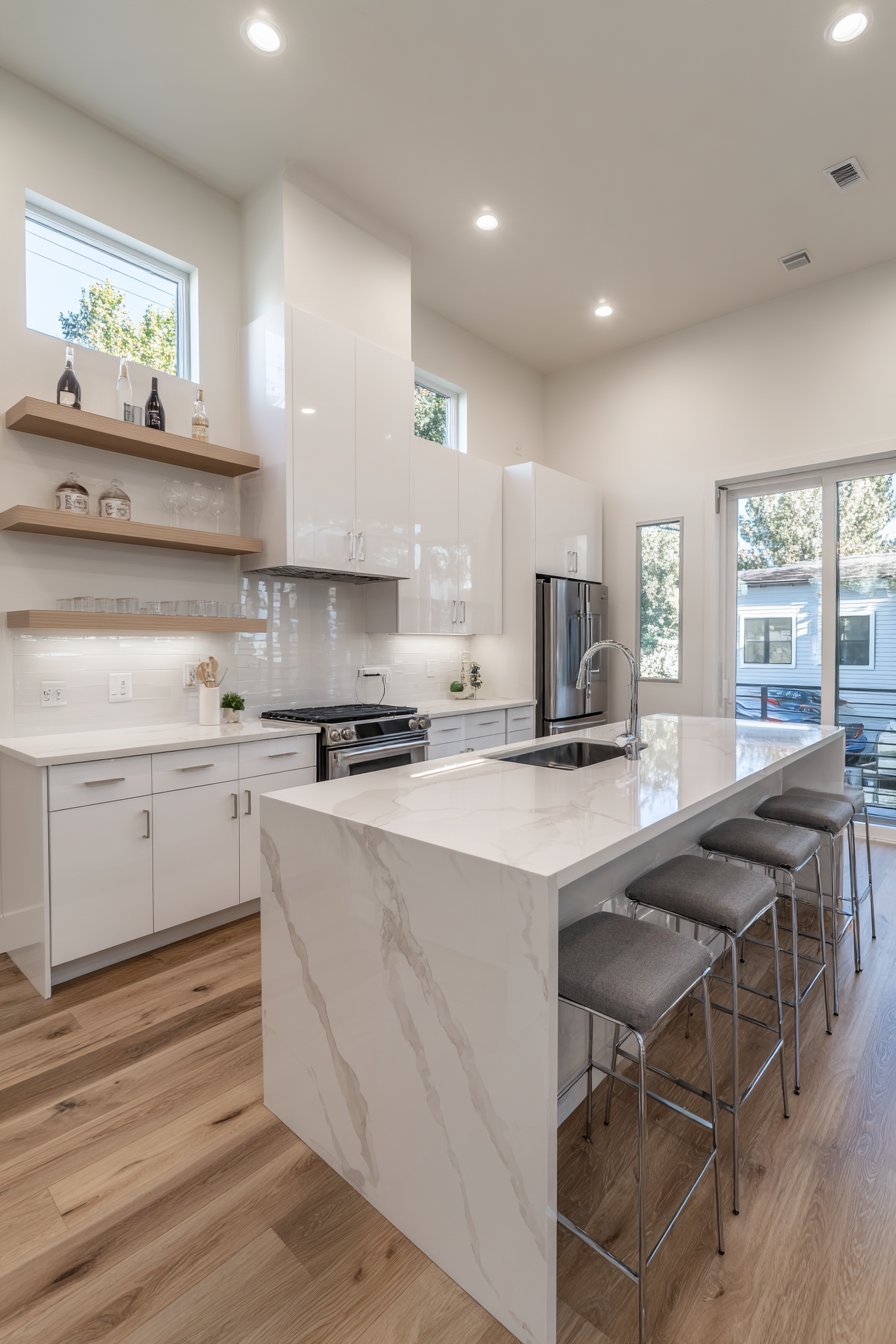 Glossy white kitchen cabinets with mirrored backsplash, wood floating shelves and quartz breakfast bar