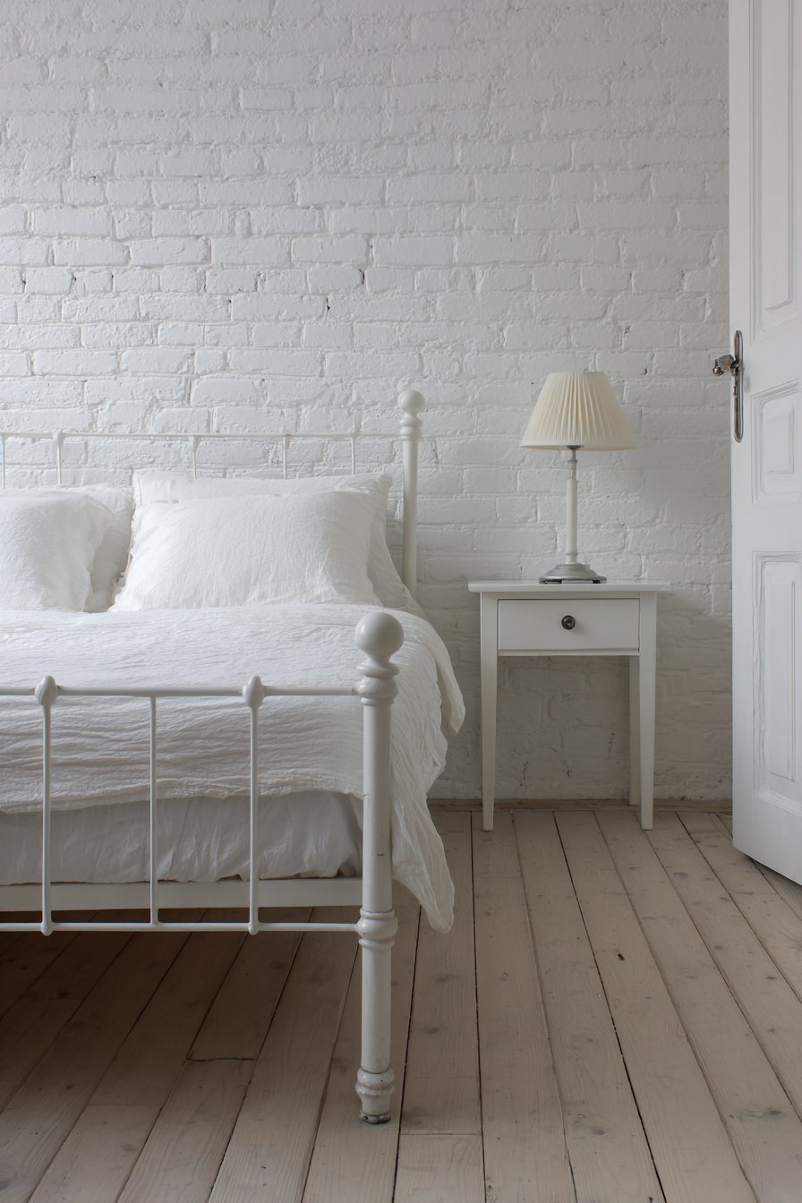 All-white small bedroom with painted brick wall, layered linen bedding and light ash wood floor