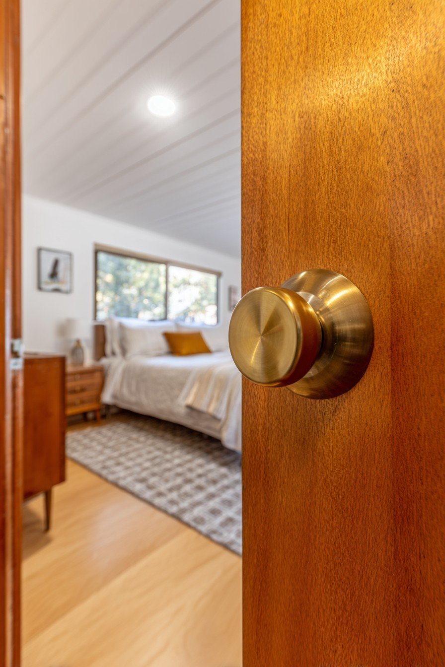 Walnut horizontal plank bedroom door with brass cylindrical knob beside a teak dresser and geometric rug