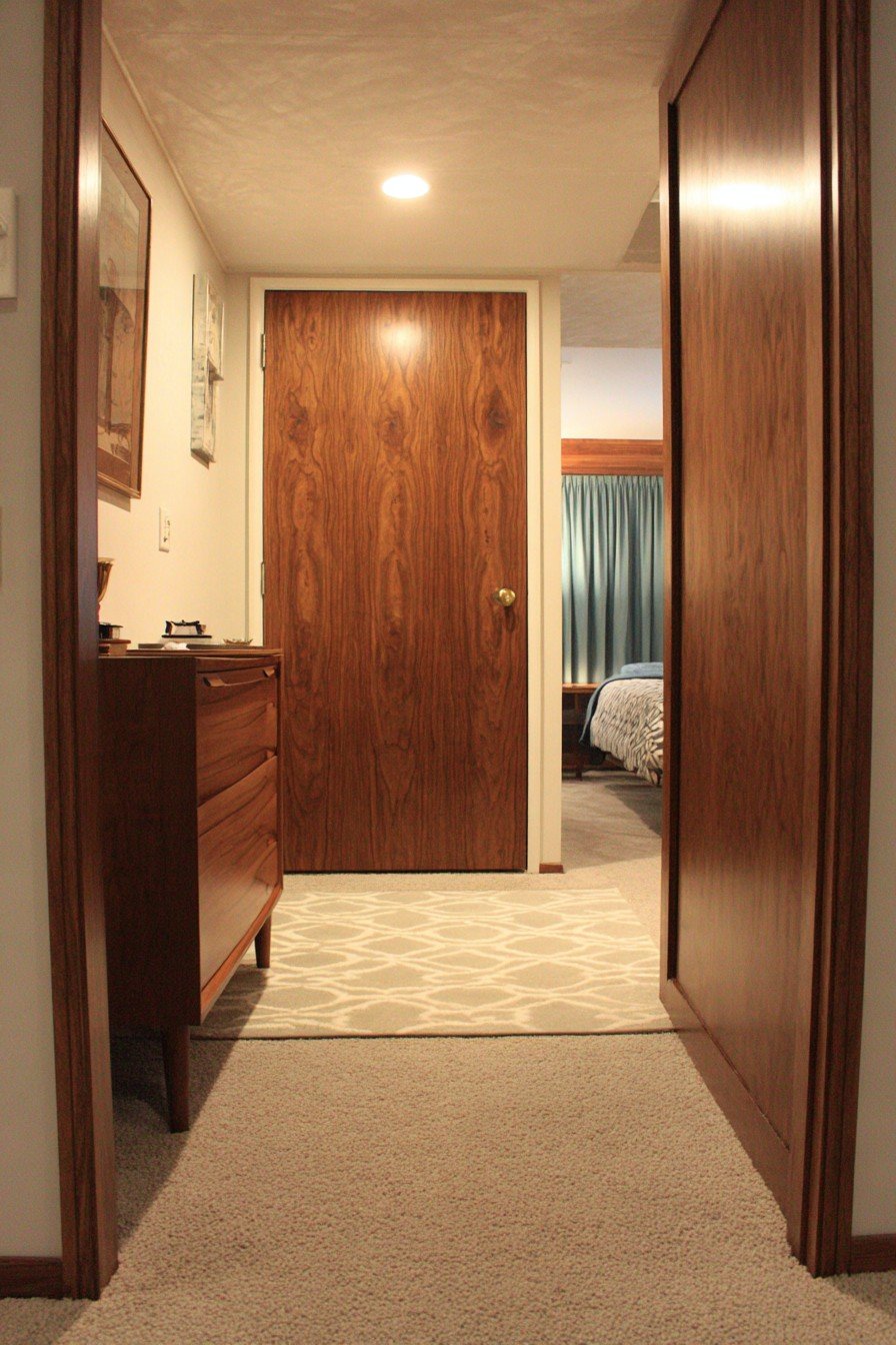 Walnut horizontal plank bedroom door with brass cylindrical knob beside a teak dresser and geometric rug
