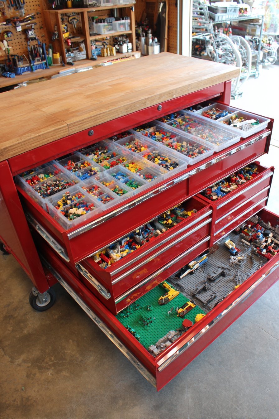 Red rolling tool chest with drawers of divided Lego trays and a work surface top in a garage workspace