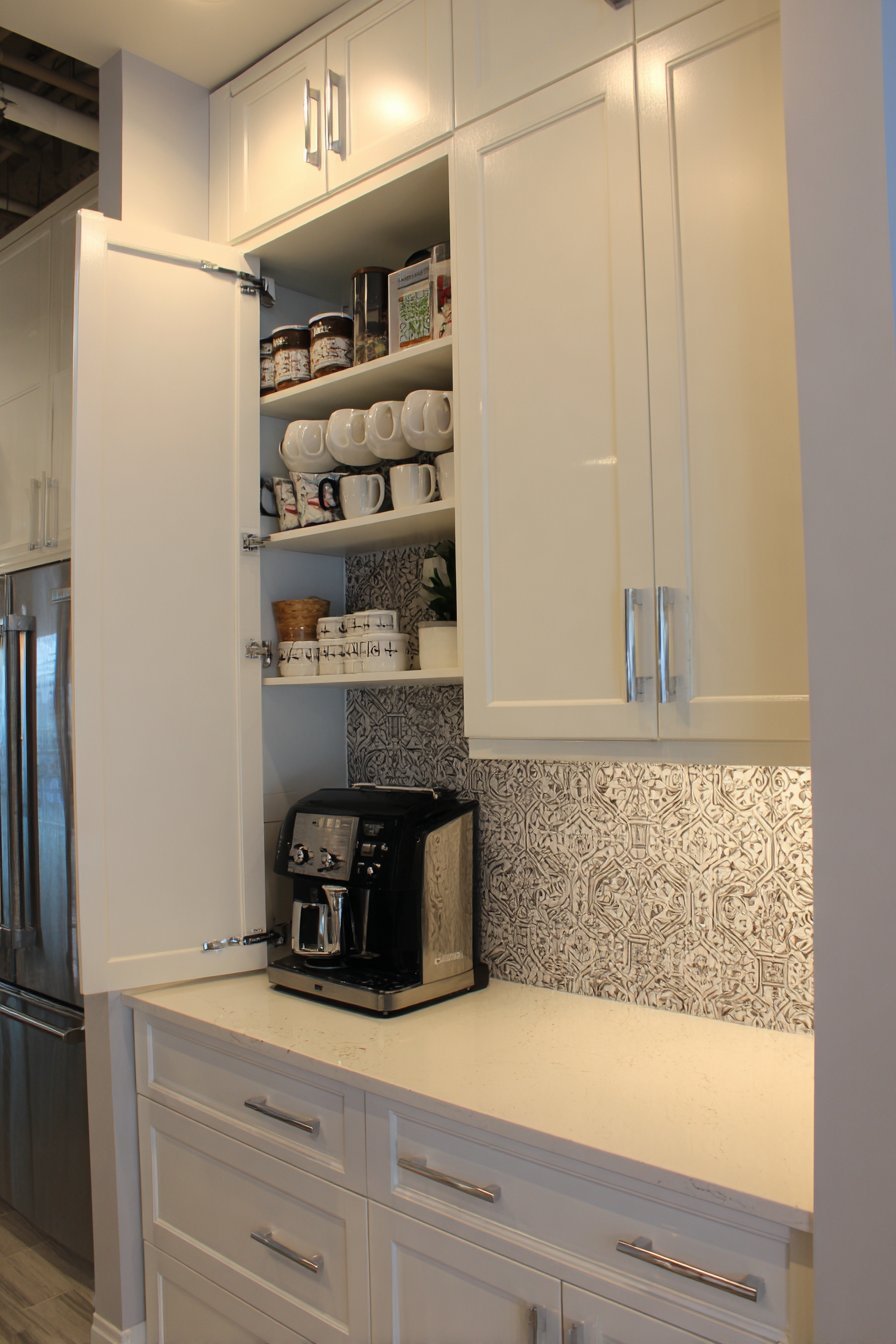 Hidden coffee station in an open cabinet with pull-out shelf, mug hooks and cement tile backsplash