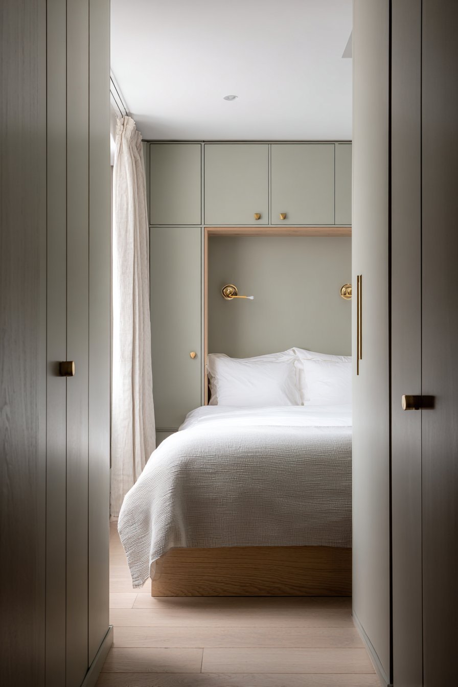 Bed set in an alcove between sage green built-in wardrobes with brass picture lights