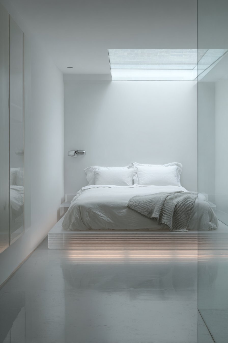 Floating white bed with LED glow beneath on polished concrete under a small skylight
