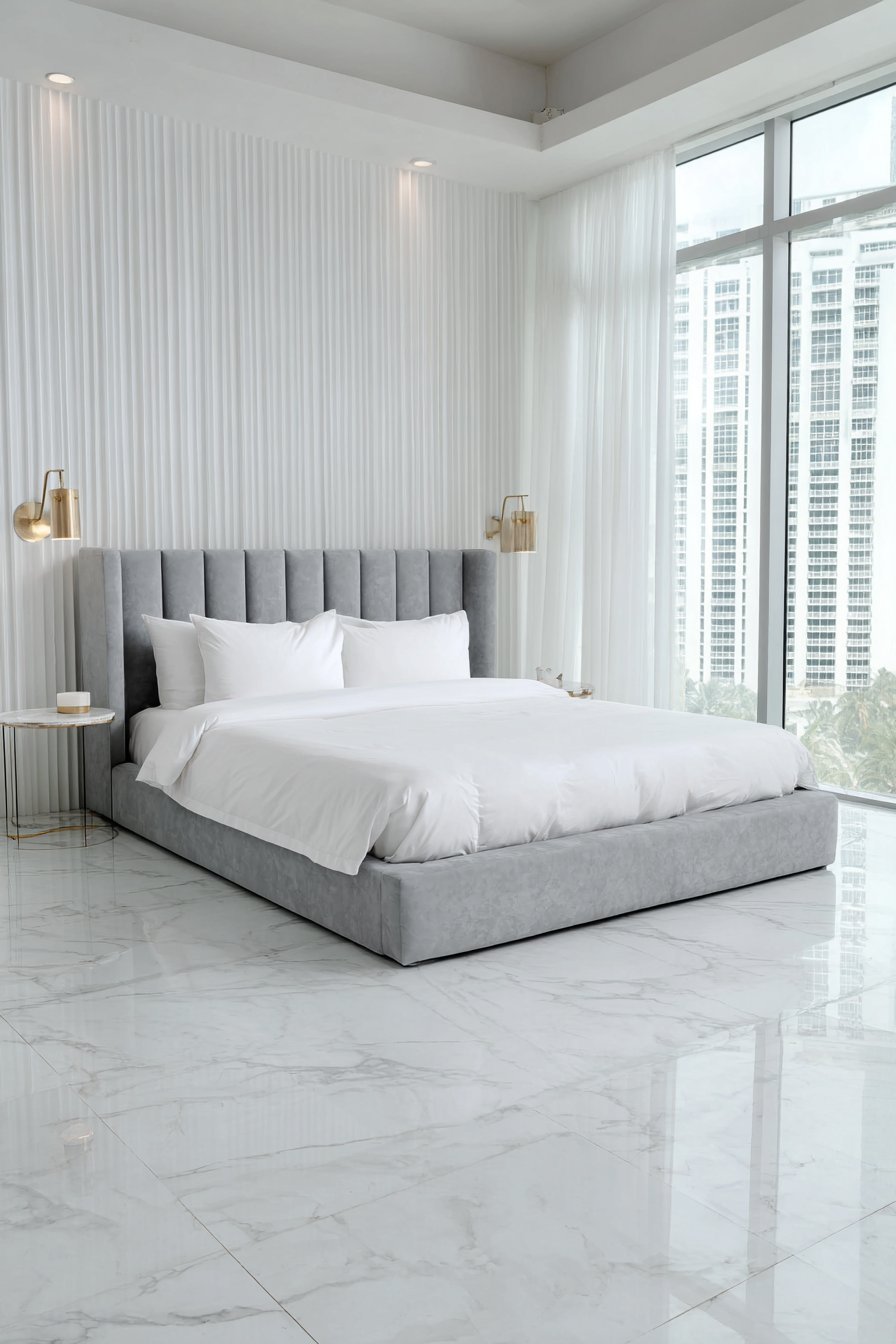 Slim ceiling-height grey velvet channel headboard, white hotel bedding, brass swing-arm lamps and white marble floor