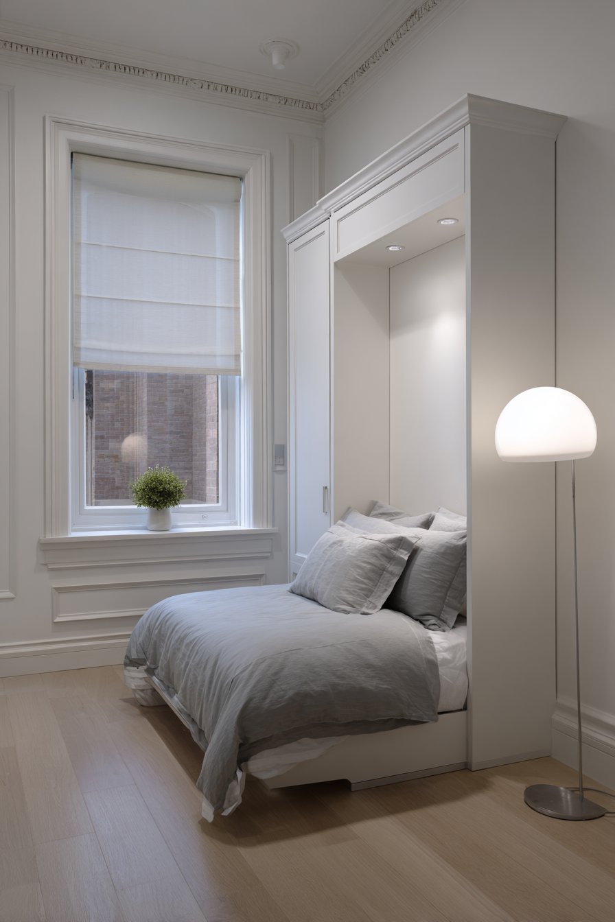 Deployed white lacquer Murphy bed with grey bedding, slim floor lamp and honeycomb shade on grey vinyl floor