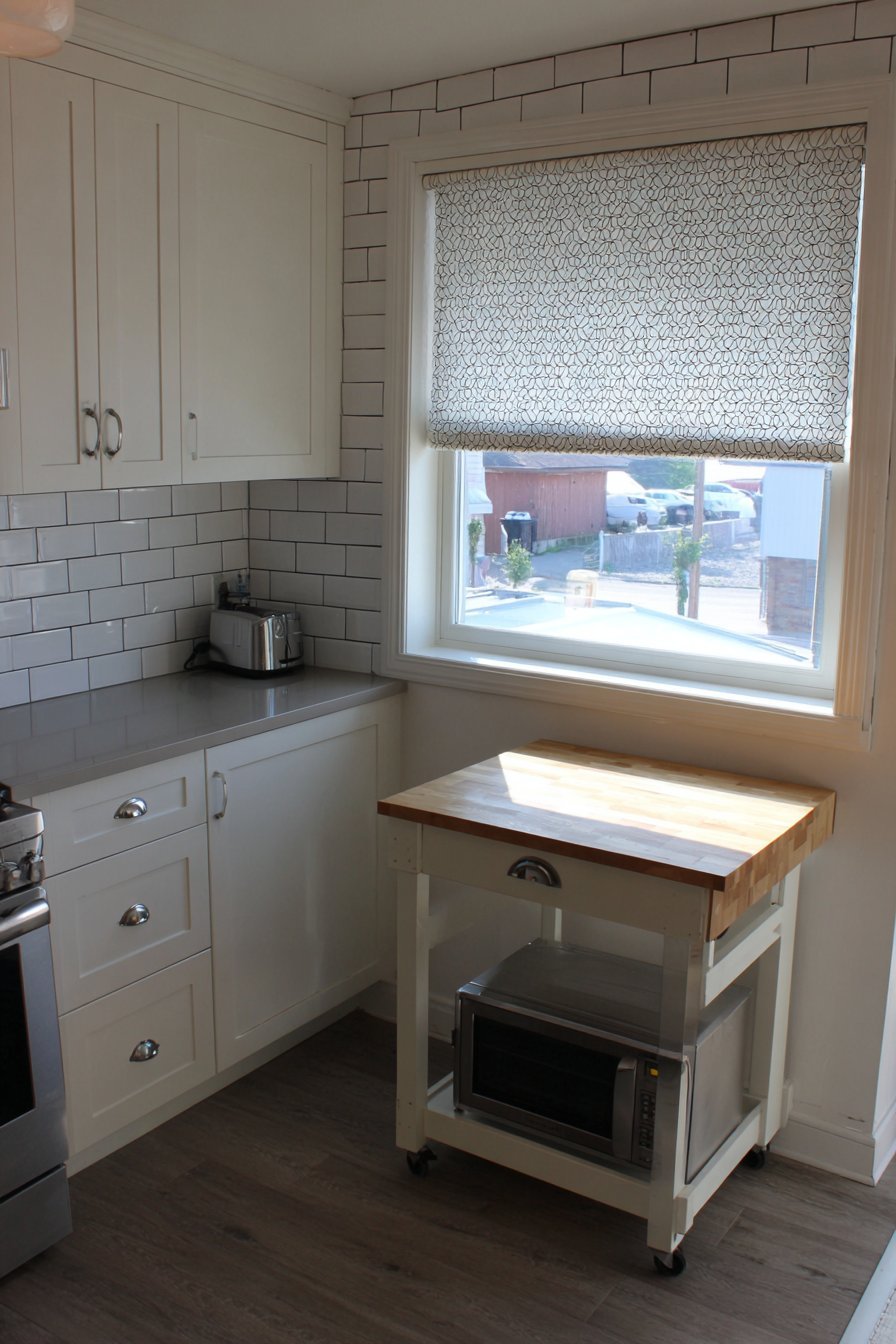 Two-tier wood kitchen cart beside white shaker cabinets and a subway tile backsplash