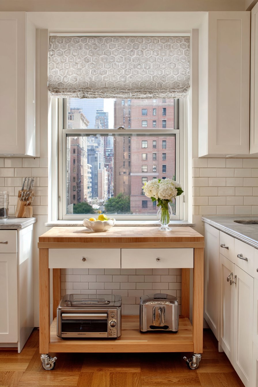 Two-tier wood kitchen cart beside white shaker cabinets and a subway tile backsplash