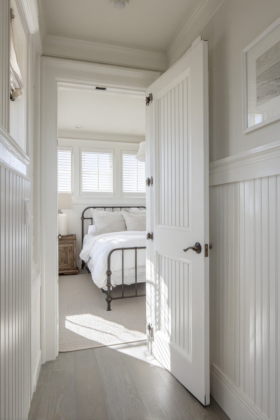 White Dutch bedroom door with beadboard panels and ceramic knobs, top half open onto an iron bed