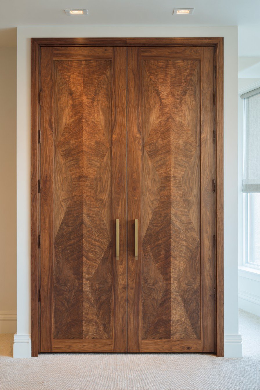 Nine-foot book-matched walnut bedroom door with recessed bronze pulls and cove lighting on white walls