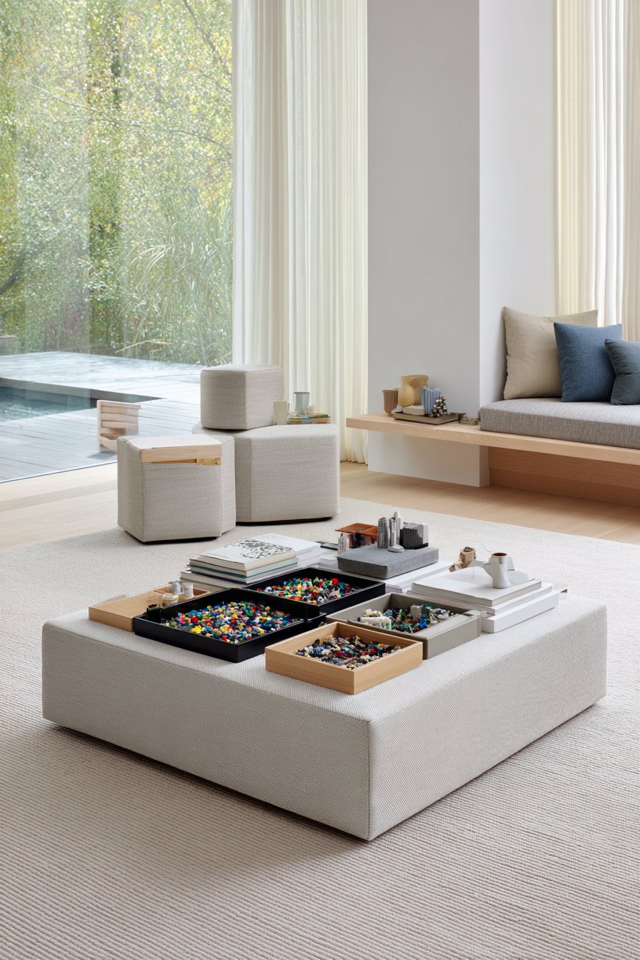Square linen ottoman with removable sectioned tray holding sorted Lego, used as a living room coffee table