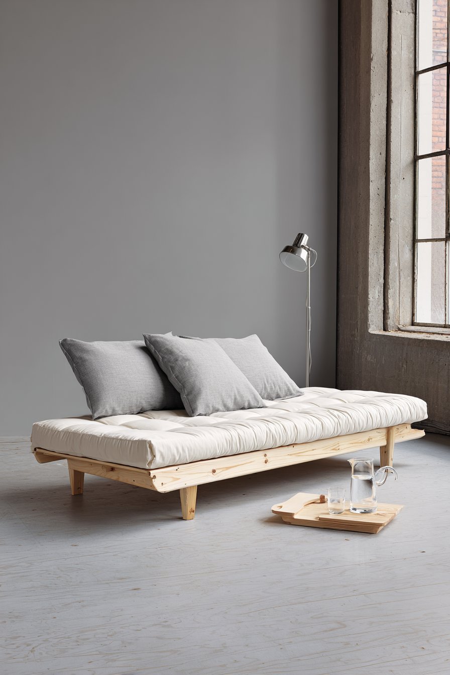 Ash wood daybed with white linen and grey bolster pillows, side table and adjustable floor lamp on cork floor