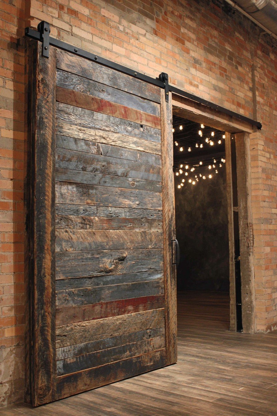 Oversized reclaimed barn wood sliding door on exposed black steel track beside an exposed brick wall