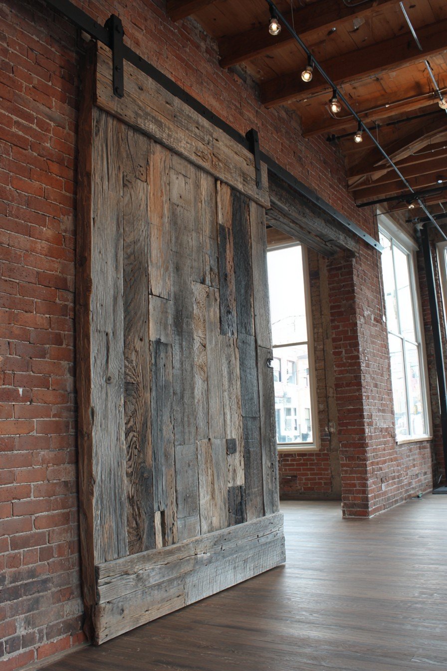 Oversized reclaimed barn wood sliding door on exposed black steel track beside an exposed brick wall