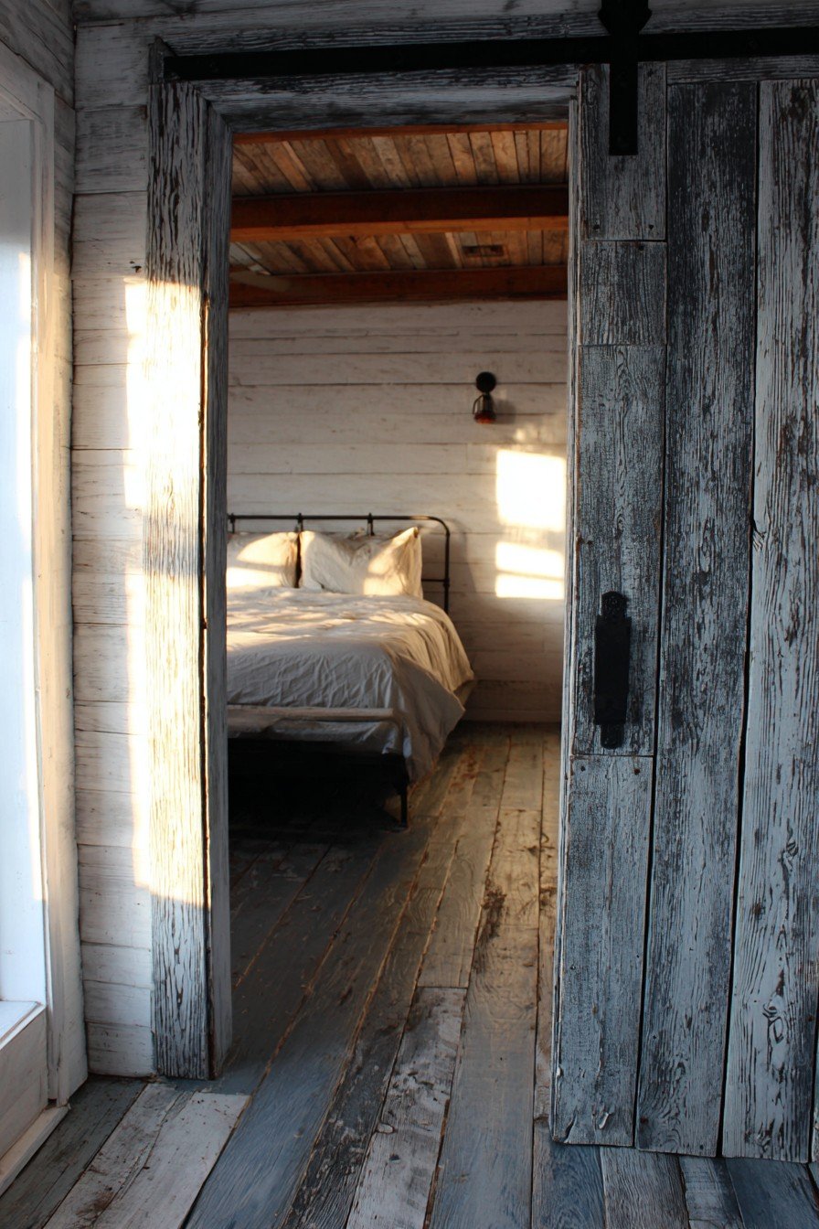 Weathered reclaimed barn wood bedroom door with iron strap hinges and thumb latch beside whitewashed shiplap