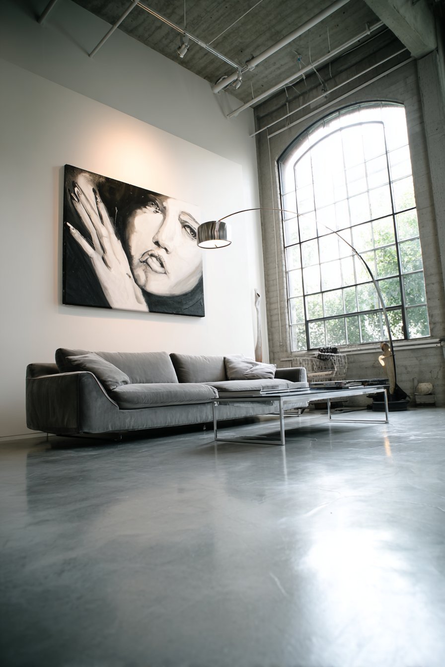 Minimalist living room with oversized black and white print above a grey velvet sofa on polished concrete