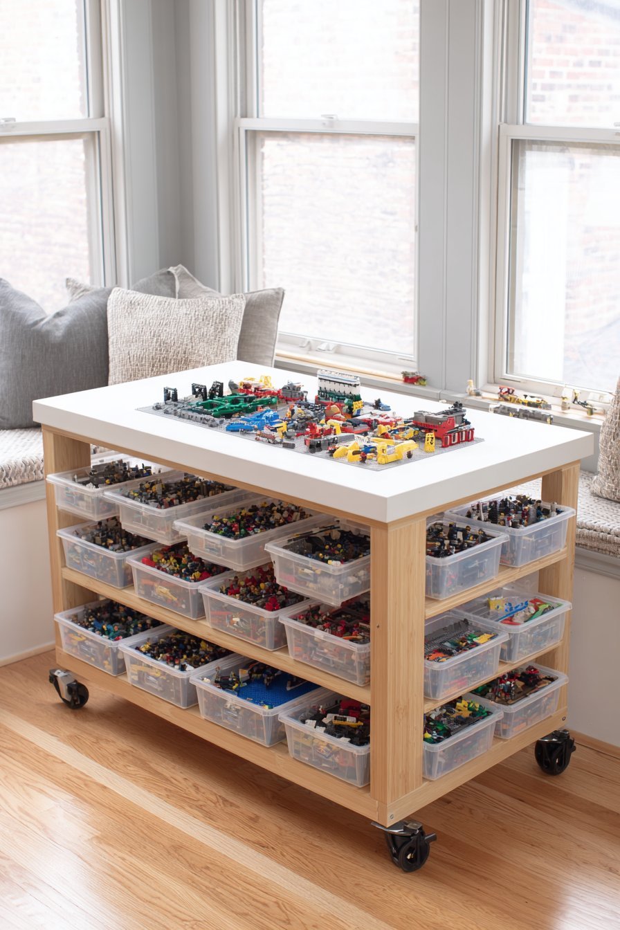Bamboo rolling cart with white laminate top, four baseplates and three tiers of Lego containers by a window seat