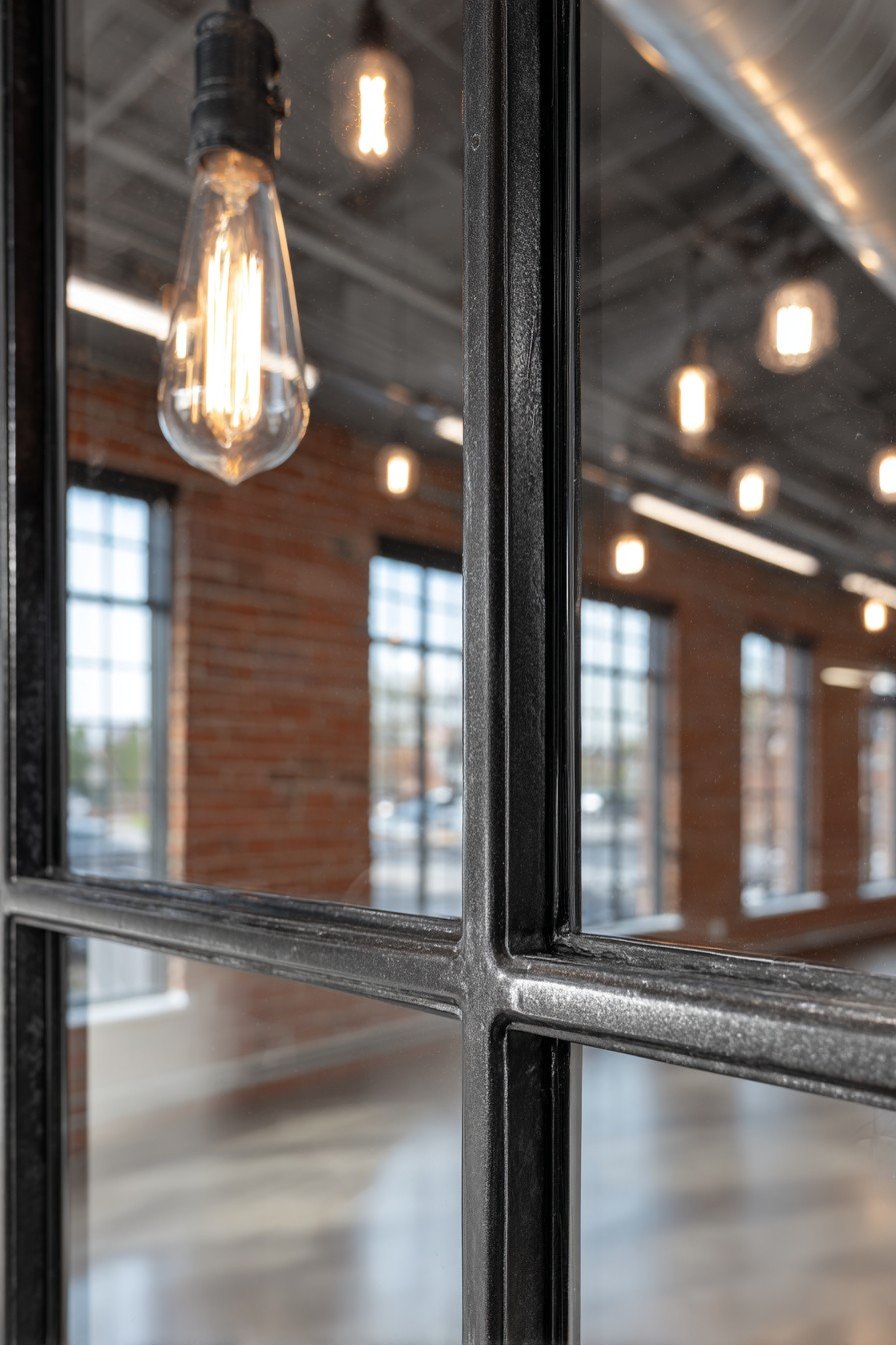 Black steel-framed glass bedroom door in a loft with exposed brick walls and Edison bulb pendants