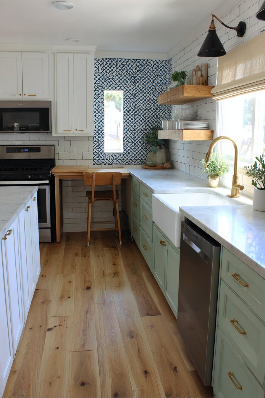 Small L-shaped kitchen with sage green lower cabinets, white uppers, brass pulls and quartz peninsula